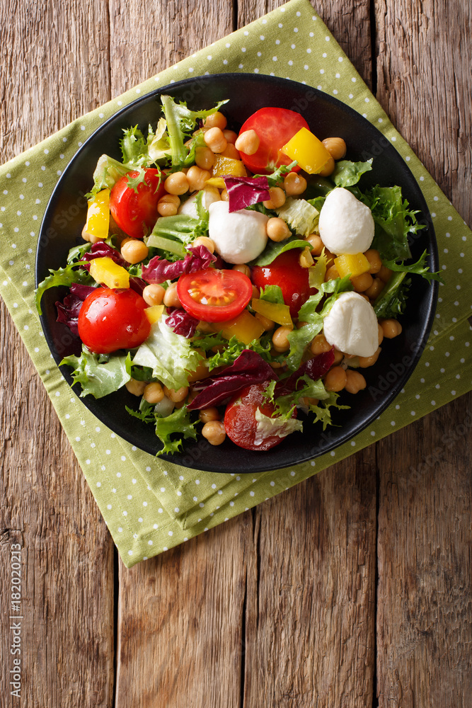 Healthy food: salad with chickpeas, vegetables and mozzarella cheese close-up. Vertical top view