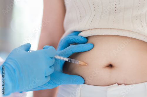Nurse or doctor in blue glove  holding a syringe with a liquid inject  to a belly of pateint in the hospital, Diabetes treatment.