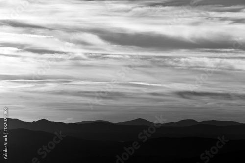 A silhouette of a mountain range at sunset, under a big cloudy sky