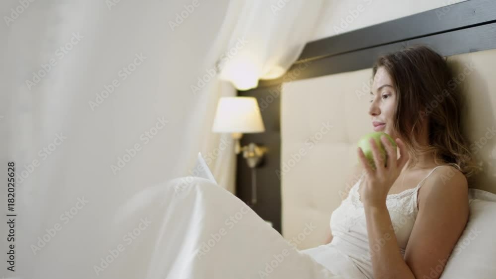 Young woman using digital tablet on bed with an appla in her hand Young woman using digital tablet on bed with an appla in her hand