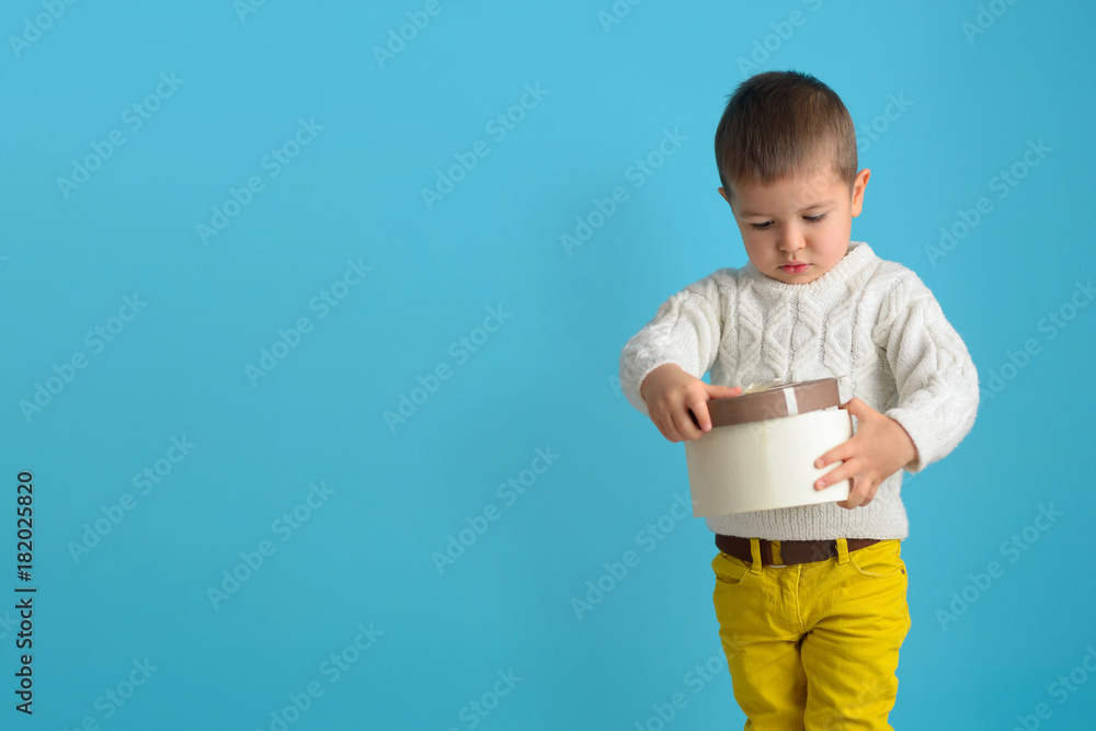 A little agitated boy is holding a gift. Child looking of a cardboard box tied with a ribbon. A little agitated boy is holding a gift. Child looking of a cardboard box tied with a ribbon.