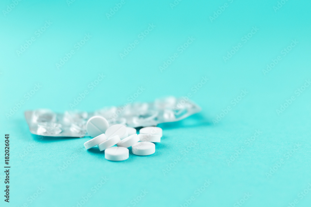 Empty pack with white pills packed in blister with copy space on turquoise background. Focus on foreground, soft bokeh. Pharmacy drugstore concept