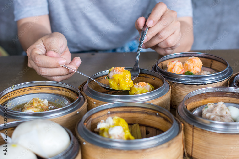 Close up Eating shrimp dumpling and varieties dim sum in bamboo basket steamer, chinese cuisine