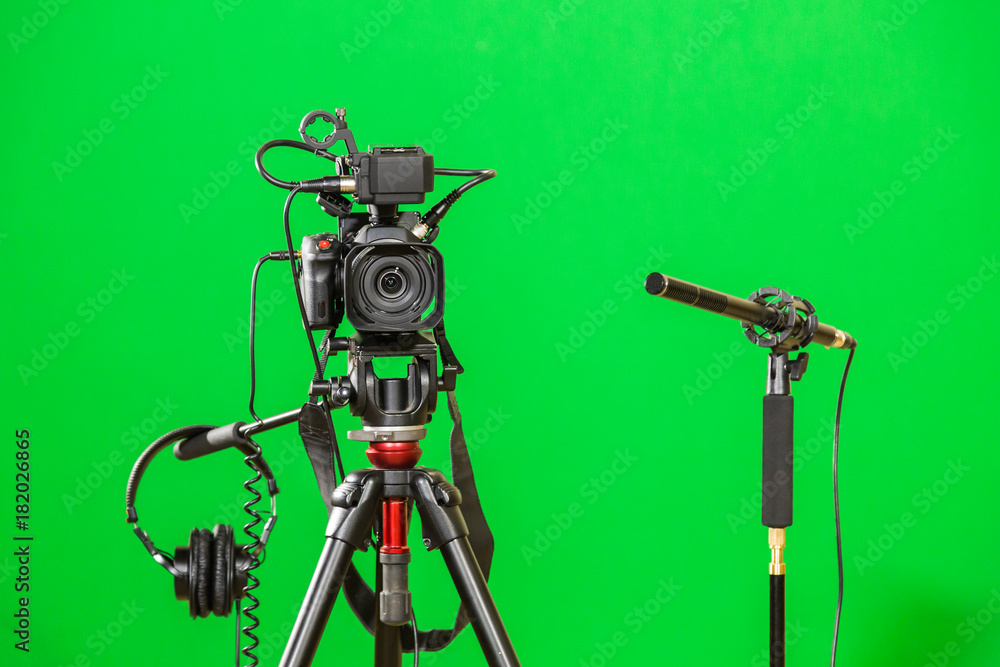 Fotografia do Stock: Video camera on a tripod, headphones and a directional  microphone on a green background. The chroma key. Green screen. | Adobe  Stock