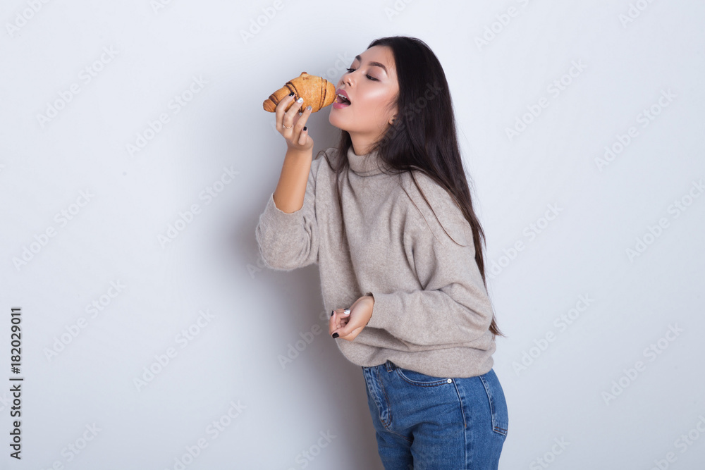 Beautiful and hungry Asian girl eating tasty croissant and smile. Breakfast isolated on white background. Happy young woman have a fun with tasty meal. Beautiful and hungry Asian girl eating tasty croissant and smile. Breakfast isolated on white background. Happy young woman have a fun with tasty meal.