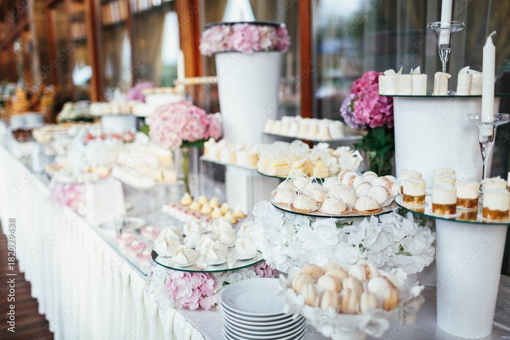 Wedding candy bar rich served with pink hydrangeas, white cookies and chocolates, eclairs and macaroons