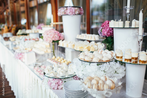 Wedding candy bar rich served with pink hydrangeas  white cookies and chocolates  eclairs and macaroons