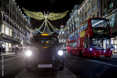 Canvas Print Red double-decker bus and black cabpass under twinkling Christmas lights along the upscale shopping district of Regent Street