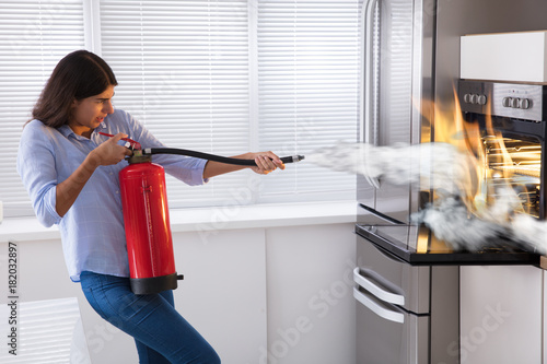Woman Using Fire Extinguisher To Put Out Fire From Oven