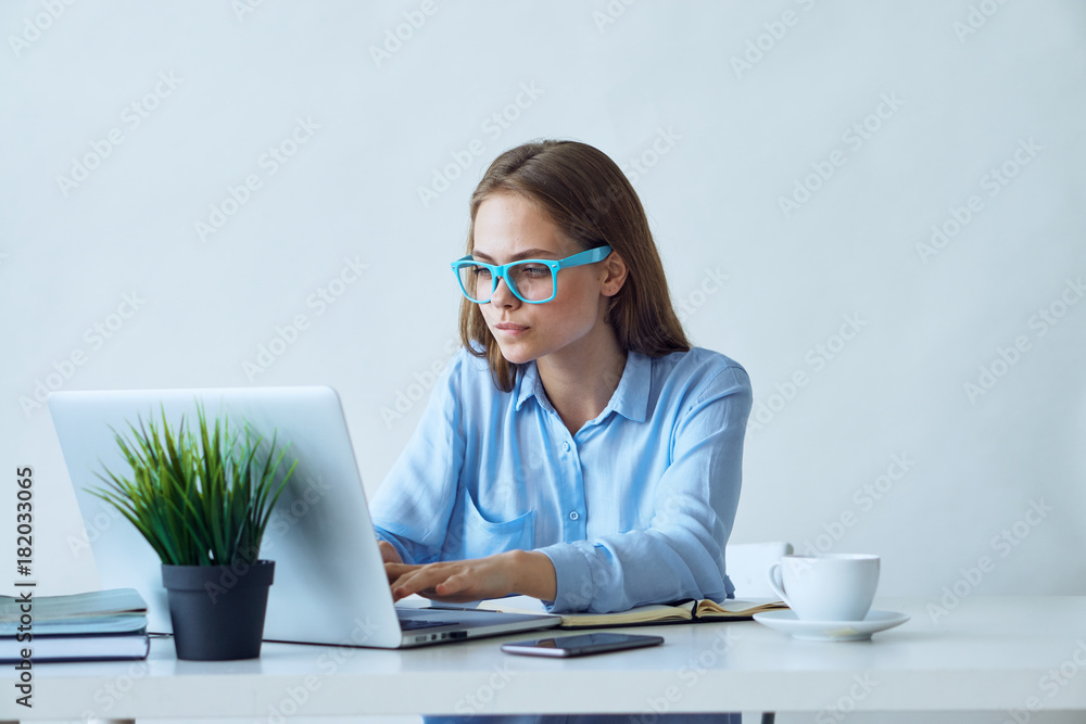 Young beautiful woman in blue glasses works at the computer in the office Young beautiful woman in blue glasses works at the computer in the office