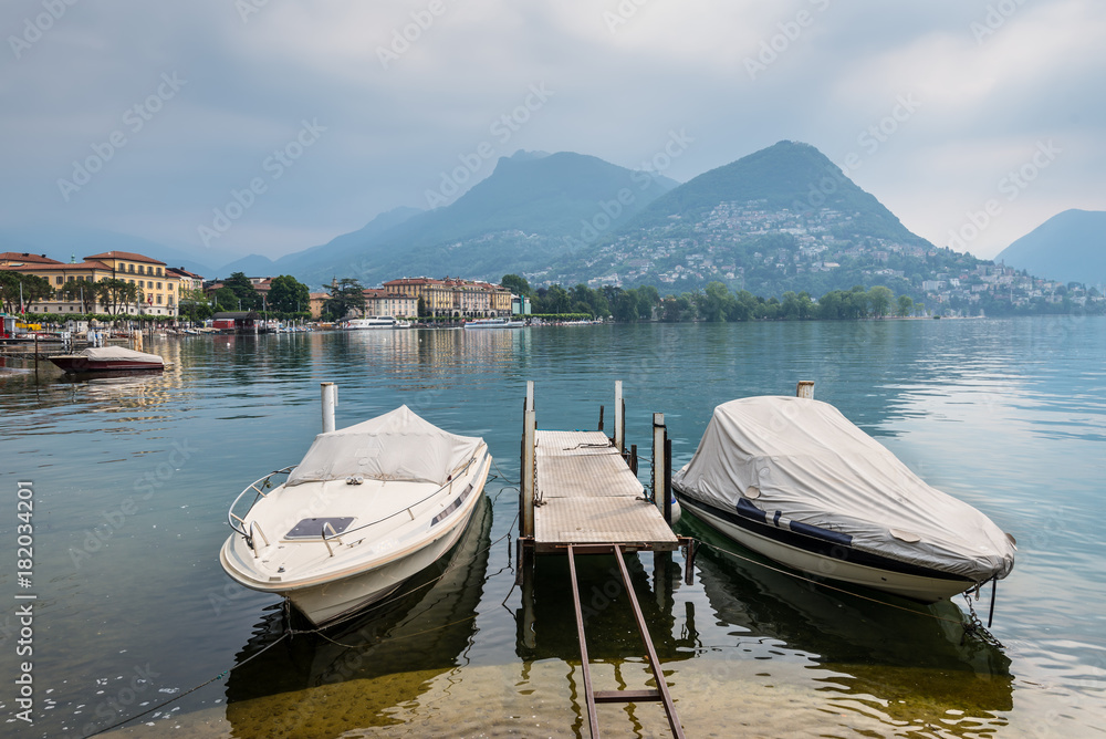 Lake and mountains in Lugano, Switzerland. Boats are moored in the foreground.