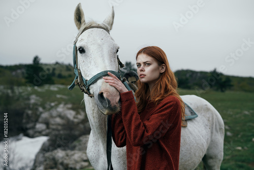 Young beautiful woman with a white horse in the mountains outdoors