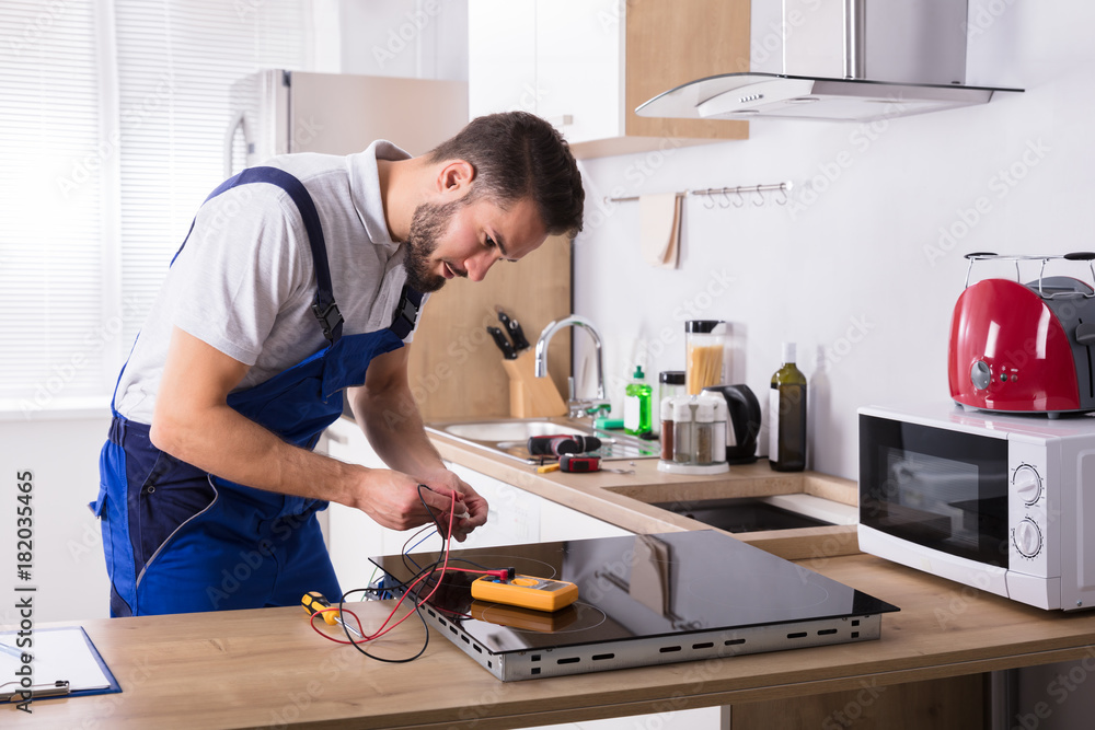 Technician Repairing Induction Stove In Kitchen Technician Repairing Induction Stove In Kitchen