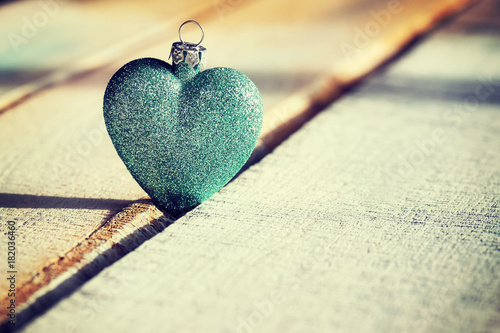 Christmas green bauble heart on a wooden background, color toned photo, selective focus.