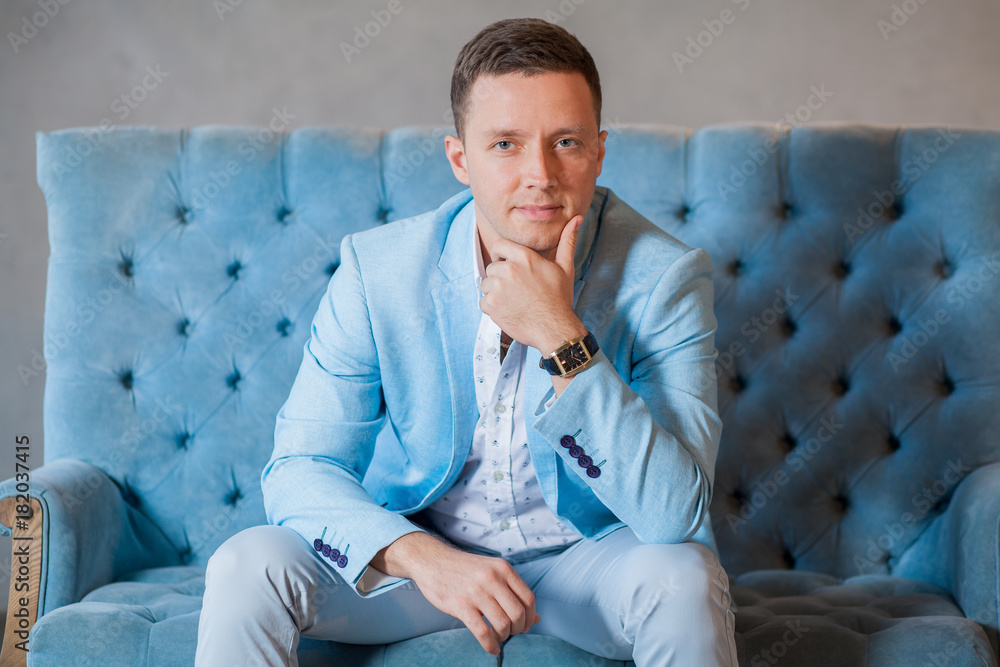 young elegant man in suit sits on arm chair