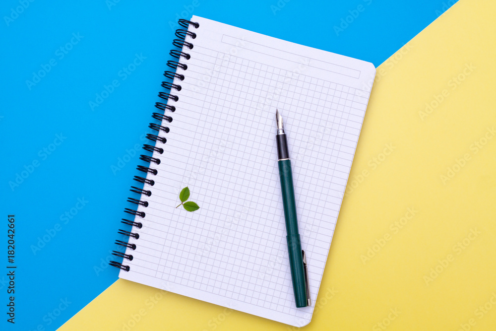 Top view on a blank notebook with pen flat lay on blue and yellow background. Top view on a blank notebook with pen flat lay on blue and yellow background.