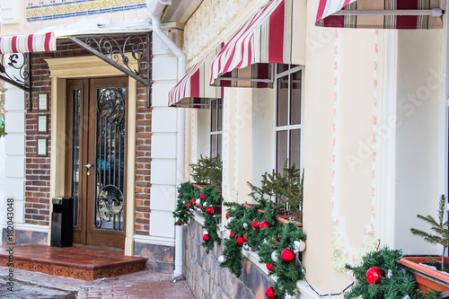 Many glittering, shiny Christmas tree balls, decoration on windows of a restaurant, cafe. Brick wall,door with metal forged elements