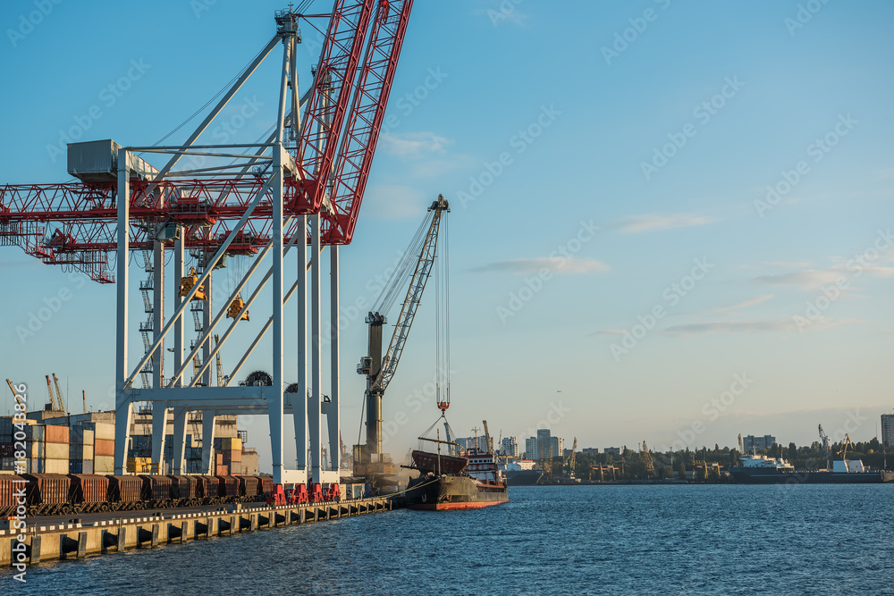 A view of the cargo port and cranes, a ship with containers at the pier. Sunny day, calm water of the sea.  Ukraine. Black Sea.
