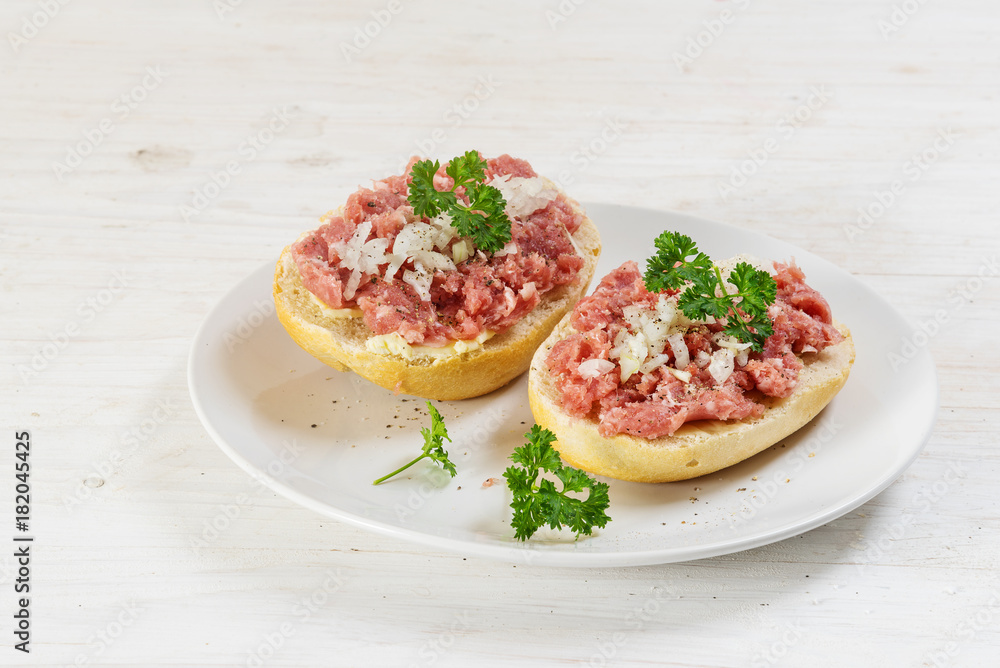 minced pork sausage, german mettwurst with onions and parsley on a bun, white plate on a white wooden table with copy space minced pork sausage, german mettwurst with onions and parsley on a bun, white plate on a white wooden table with copy space