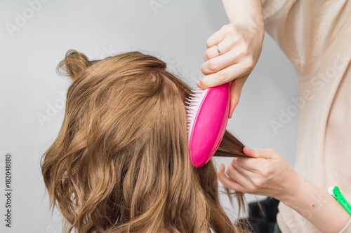 hairdresser making preparation for a ginger woman in a beauty salon combing her hair with brush