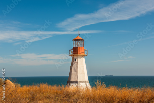 Lighthouse on the wild cliff of the sea among the yellow grass. Beautiful sunny sea view. 