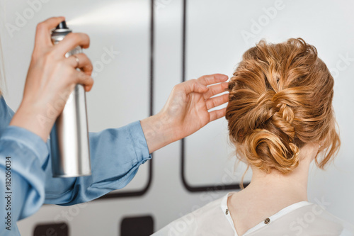 An coiffeur in the hairdressing salon makes a hairstyle and fixes it with a spray