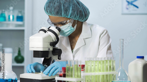 Woman scientist looking into microscope, biochemical research, cosmetology photo
