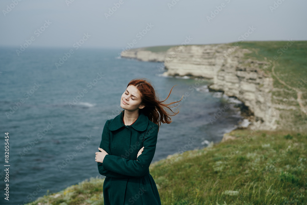 Young beautiful woman on a cliff of a mountain near the sea, the wind