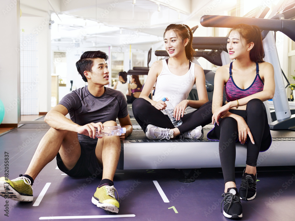 asian young people resting and talking in gym asian young people resting and talking in gym