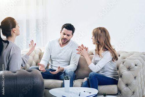 It is enough. Smart professional female psychologist looking at the couple and stopping their argument while having a psychological session with them