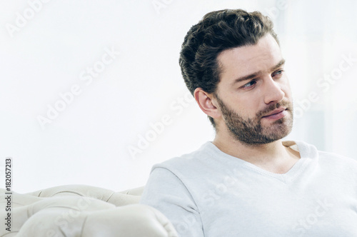 Handsome man. Portrait of a pleasant nice bearded man while sitting on the sofa and thinking about his life