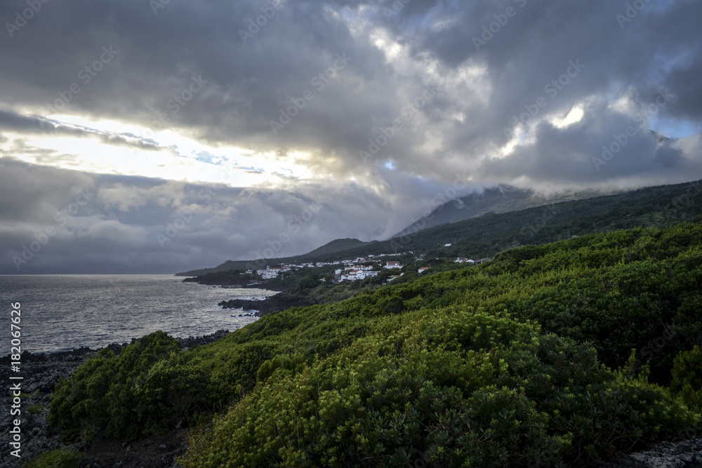 lava coastline with a volcano under a dramatic sky at sunset on the island of Pico on the azores