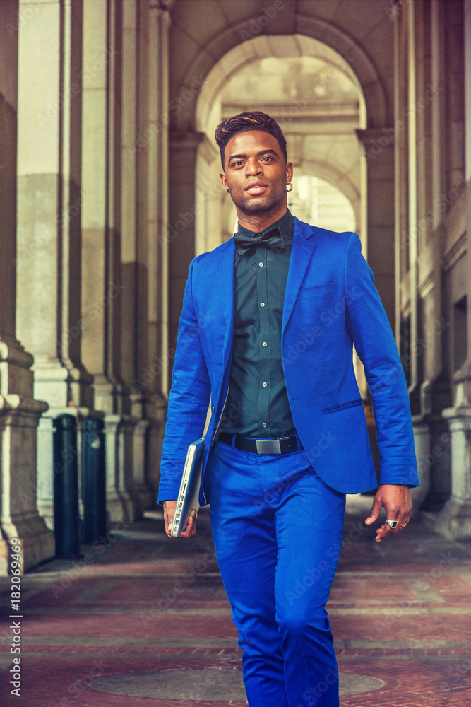 African American Man Fashion in New York. Wearing blue suit, black shirt,  bow tie, holding laptop