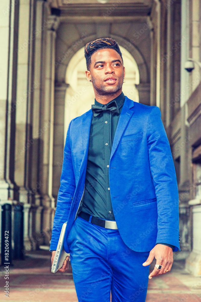 African American Man Fashion in New York. Wearing blue suit, black shirt,  bow tie, holding laptop