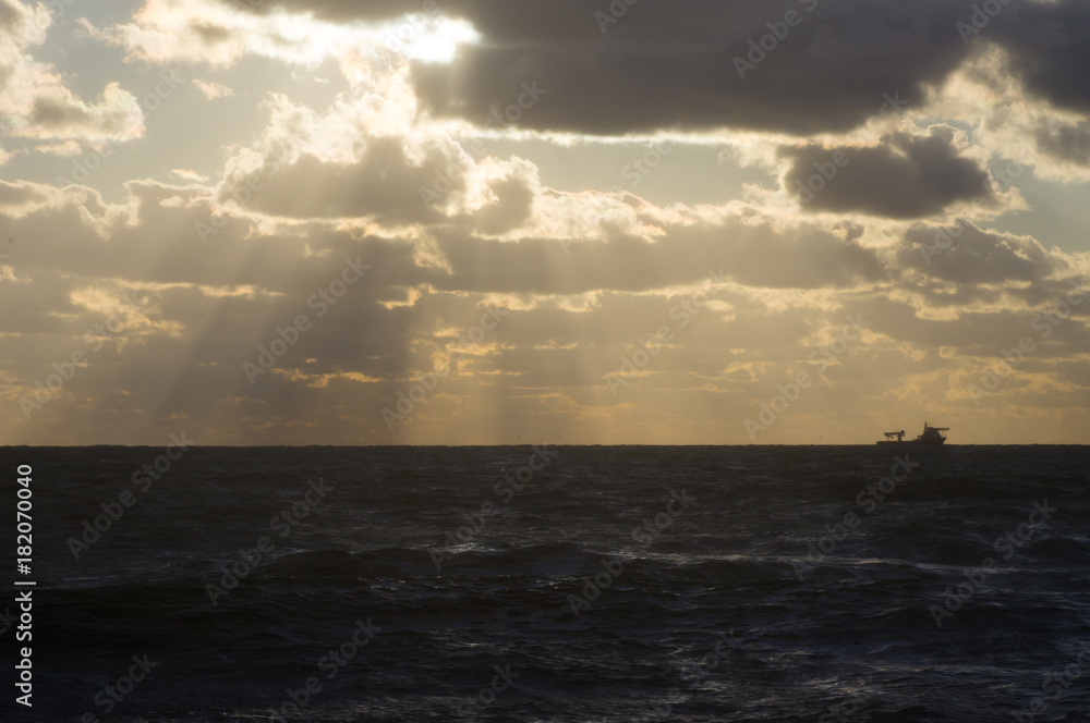 The contour of the ship on the horizon in the stormy sea at sunset in the cloudy sky
