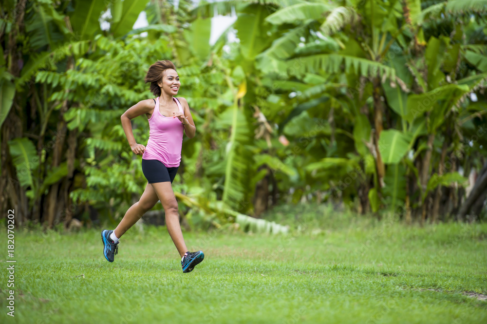 young attractive Asian sport runner woman running in the jungle smiling happy in training workout on herb with palm trees on the background young attractive Asian sport runner woman running in the jungle smiling happy in training workout on herb with palm trees on the background