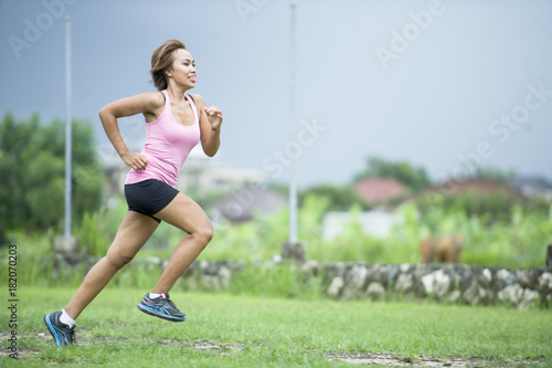 young attractive Asian sport runner woman running in the jungle smiling happy in training workout on herb background in fitness