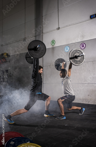 Motivational wide shot of young men holding barbells overhead