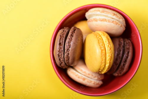Lemon, vanilla and chocolate french macarons in the red bowl on the yellow background. photo