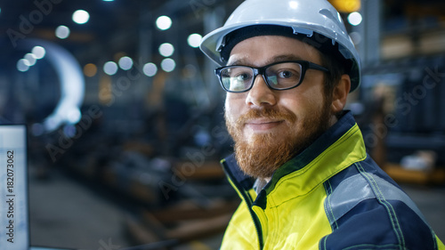  Industrial Engineer Wearing Hard Hat,  Safety Jacket and Glasses Smiles on Camera. He Works in Big Heavy Industry Factory.