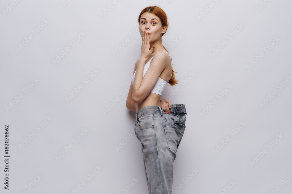 Fototapeta premium A woman in big jeans dropped weight on a gray background