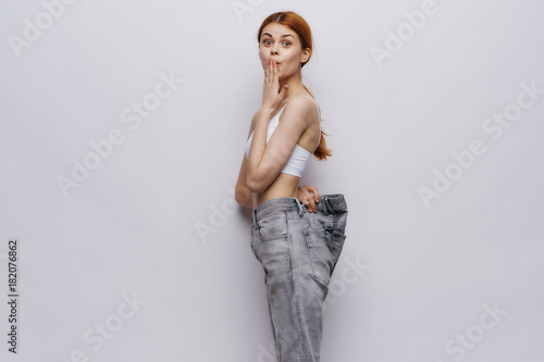 A woman in big jeans dropped weight on a gray background