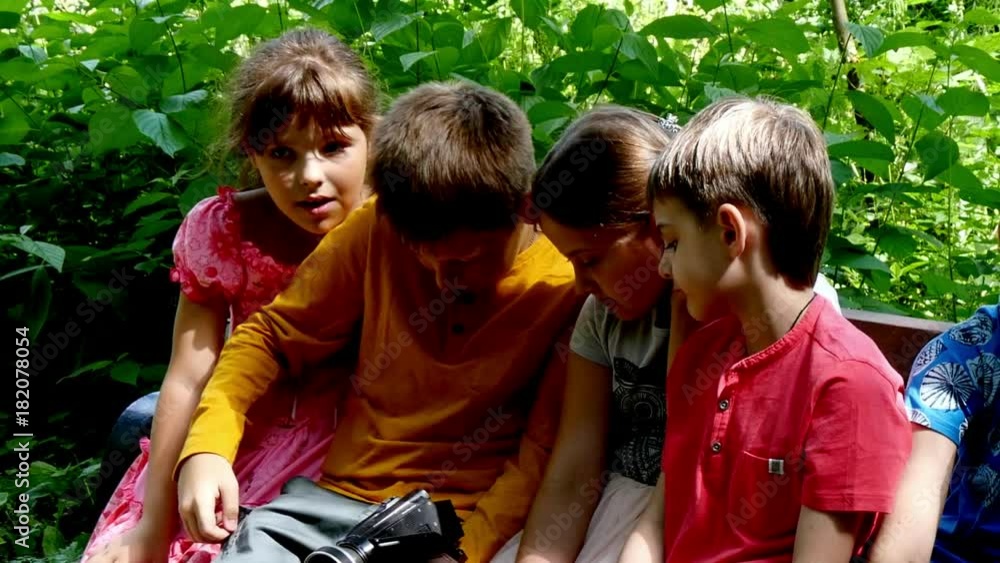 Children with video camera on bench in a green park slow motion. Young girls and boys outdoors in summer are creative work of cinema. Beautiful footage. Interesting to look at world in childhood. Children with video camera on bench in a green park slow motion. Young girls and boys outdoors in summer are creative work of cinema. Beautiful footage. Interesting to look at world in childhood.