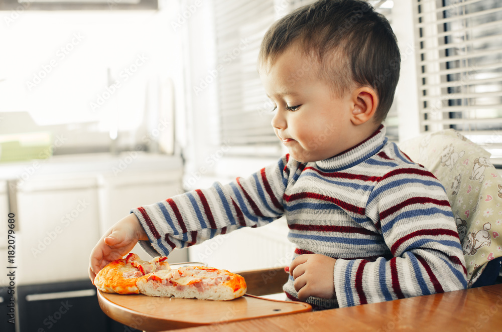 The little boy in the kitchen eating a small pizza The little boy in the kitchen eating a small pizza