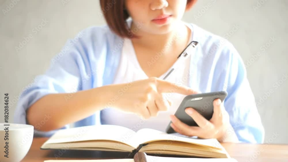Businesswoman use mobile phone and writing report on wooden table. Asian woman using phone and cup of coffee. Freelancer working in coffee shop. Woking outside office lifestyle. Businesswoman use mobile phone and writing report on wooden table. Asian woman using phone and cup of coffee. Freelancer working in coffee shop. Woking outside office lifestyle.