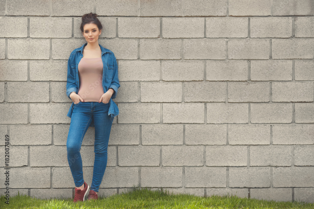 Fashion woman in denim standing near empty brick wall