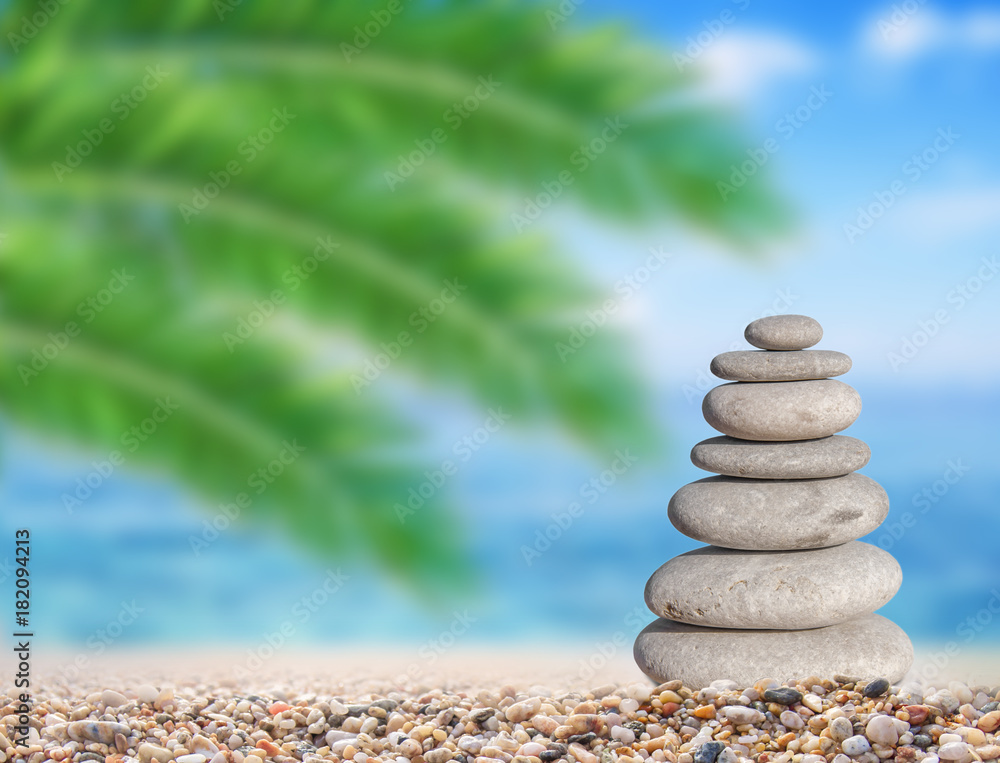 Small beach stone on beach like symbol of balance with green palm leaf background Small beach stone on beach like symbol of balance with green palm leaf background