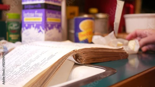 Woman cutting up butter while reading an old cookbook or recipe book in kitchen photo