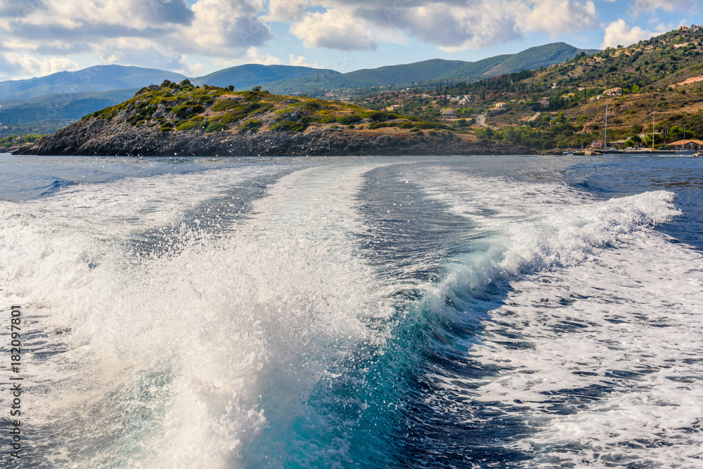 Water trail foaming behind a cruise boat. Coast  of Zakynhos island in background. Greece.