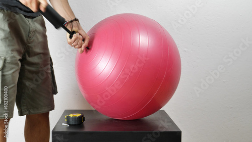 Crop shot of man pumping red fitness ball with small air pump. 